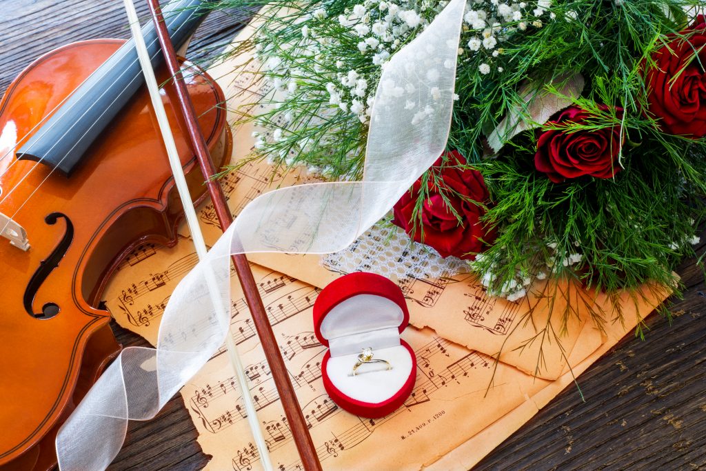 Marriage proposal with gold ring, red roses and violin on music notes